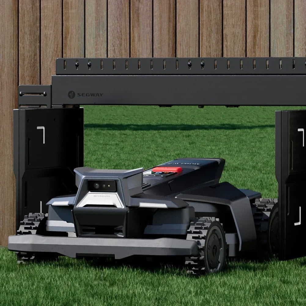 Robotic lawn mower in a grassy area with a wooden fence in the background