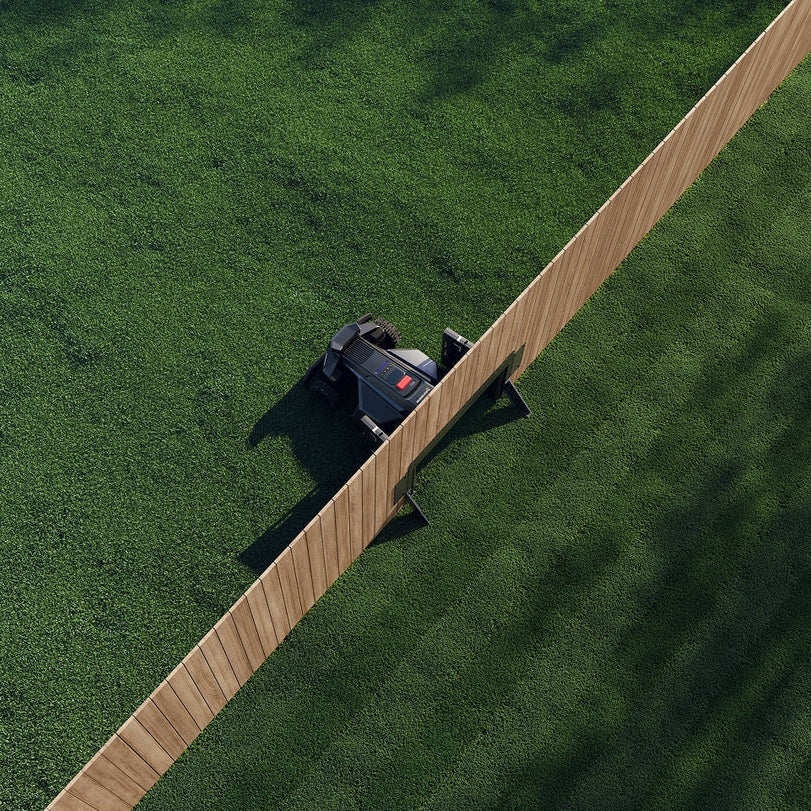 Robotic lawn mower on a green lawn with a wooden deck.
