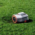 A robotic lawnmower with a gray body and bright orange wheel accents, shown operating on a green grass lawn.