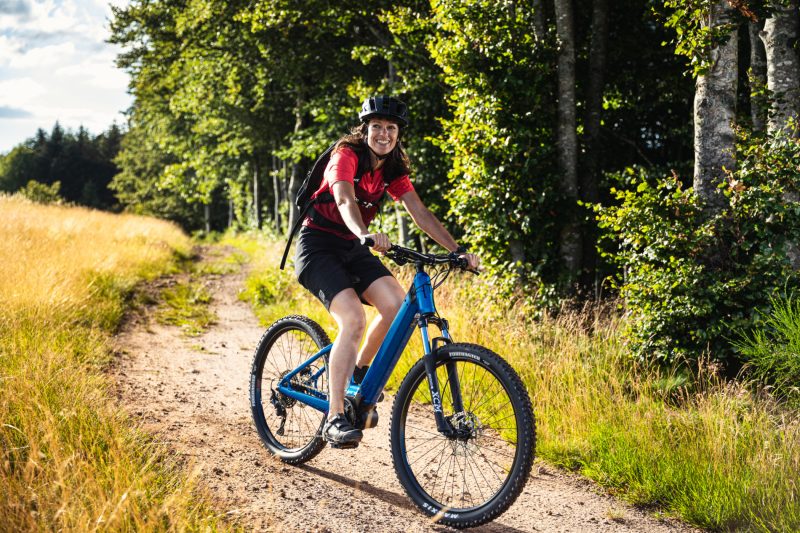 Person riding a blue electric bike on a dirt path in a forest